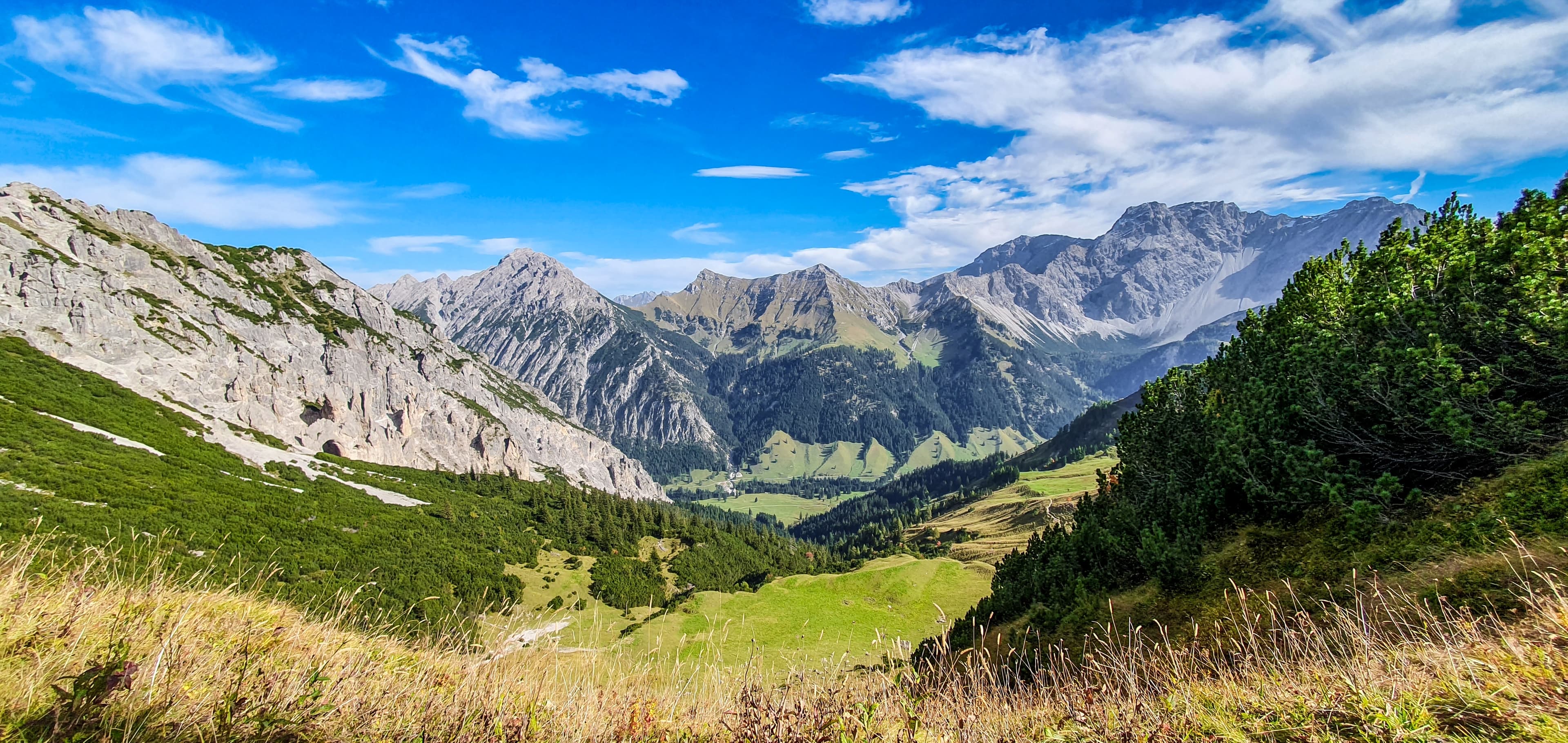 View of the picturesque mountain landscape in Malbun with lush green meadows, steep rocks, and clear blue sky.